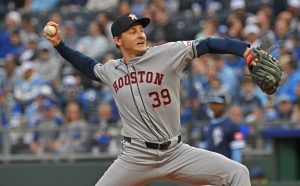A Houston baseball player in a gray jersey, number 39, winds up to pitch on a field packed with fans in the background.
