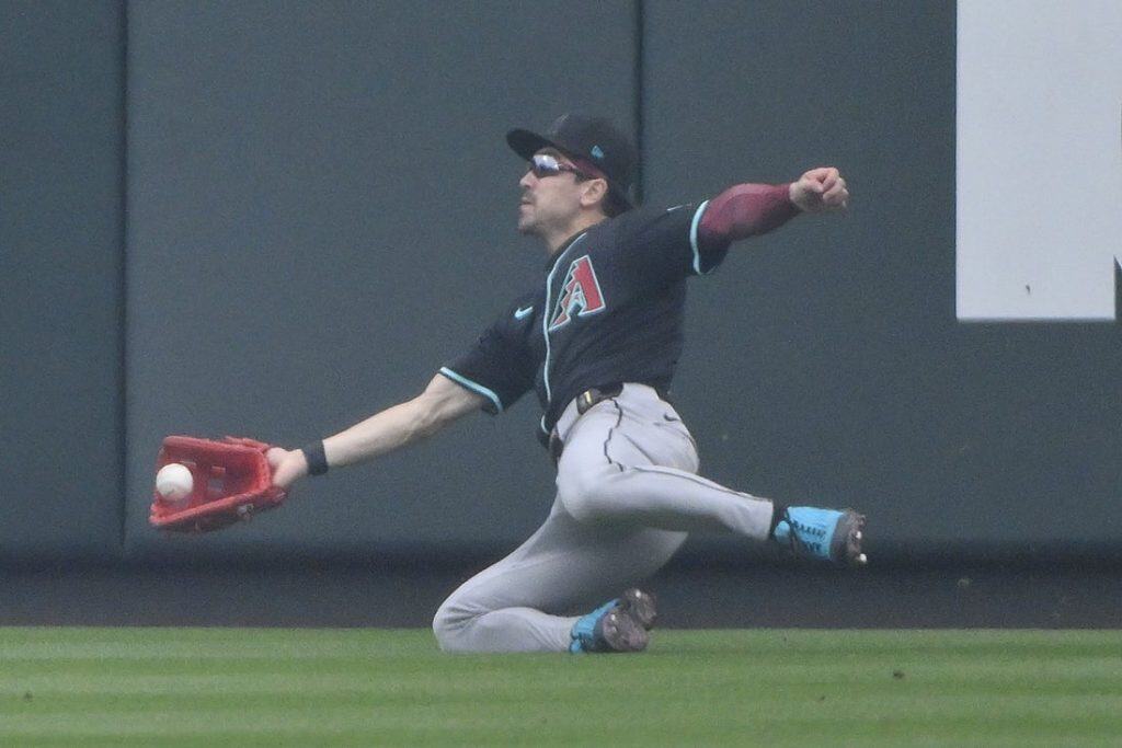 A baseball player in a black jersey dives to catch a ball, showcasing athleticism and determination on the field.
