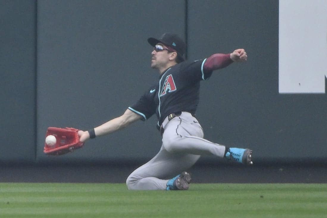 A baseball player in a black jersey dives to catch a ball, showcasing athleticism and determination on the field.