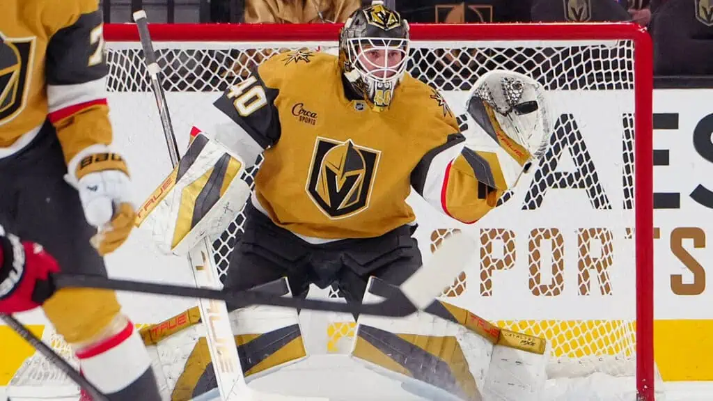 A hockey goalie in a golden jersey makes a save against the backdrop of a rink