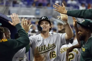 A baseball player in a gray jersey celebrates with teammates in the dugout, exchanging high-fives after a successful play.