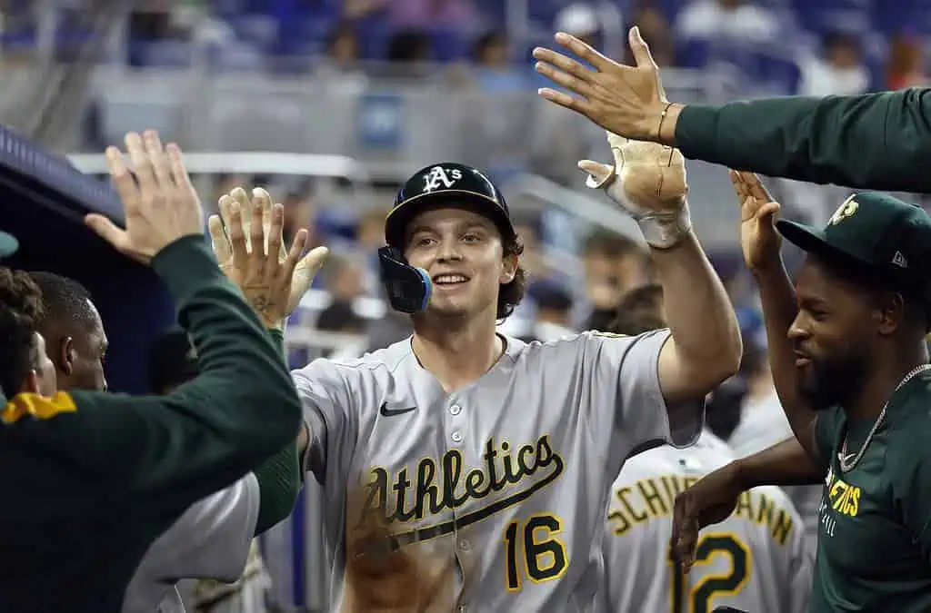 A baseball player in a gray jersey celebrates with teammates in the dugout, exchanging high-fives after a successful play.