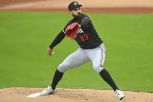 A baseball pitcher in mid-throw, wearing a black jersey with '49' on it and gray pinstripe pants, on a green field.