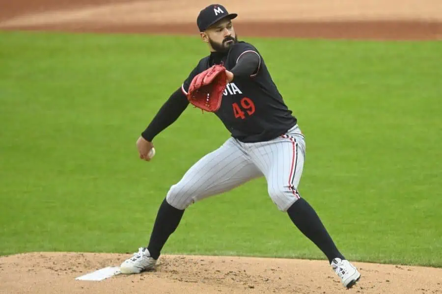 A baseball pitcher in mid-throw, wearing a black jersey with '49' on it and gray pinstripe pants, on a green field.