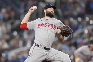 A Boston Red Sox pitcher in grey uniform winds up to throw a baseball during a night game