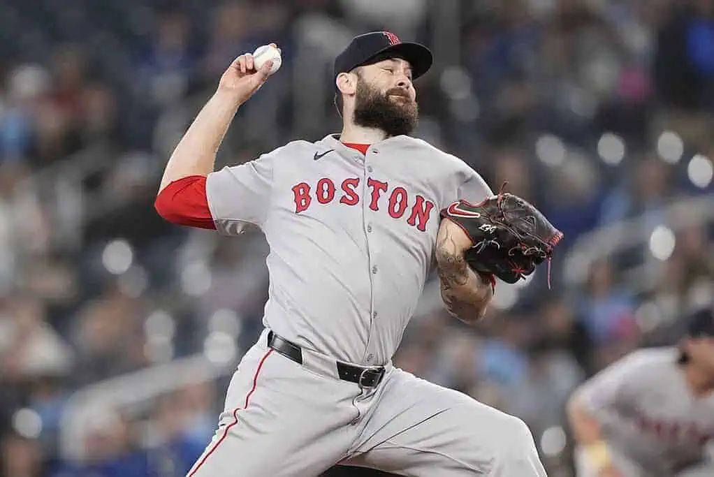 A Boston Red Sox pitcher in grey uniform winds up to throw a baseball during a night game