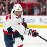 NHL action shot featuring a Washington Capitals player taking a powerful shot during a game against the Carolina Hurricanes.