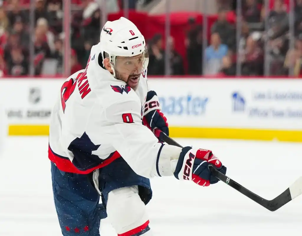 NHL action shot featuring a Washington Capitals player taking a powerful shot during a game against the Carolina Hurricanes.
