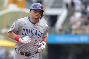 A Chicago Cubs player runs the bases, wearing a gray jersey with "CHICAGO" and the number 27, on a sunny ballpark day.