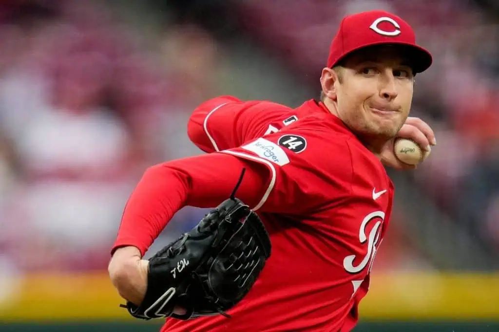 A Cincinnati Reds pitcher in a red uniform winds up to throw a baseball during a game, showcasing intensity and focus.