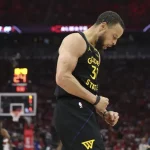 A basketball player in a Golden State Warriors jersey celebrates a successful play during an intense game, fans cheering in the background.