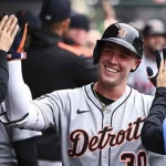 A baseball player in a Detroit Tigers jersey celebrates with teammates in the dugout, exchanging high-fives, showcasing team spirit.