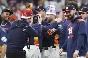 A celebration among Houston Astros players, with one wearing a colorful bucket on their head and others smiling around them.