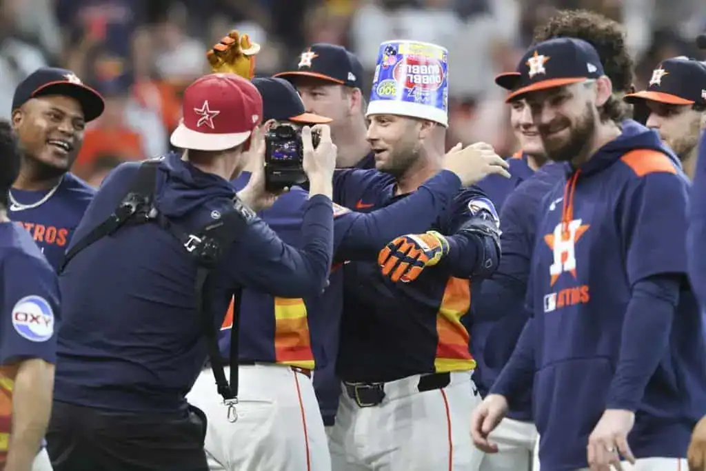 A celebration among Houston Astros players, with one wearing a colorful bucket on their head and others smiling around them.