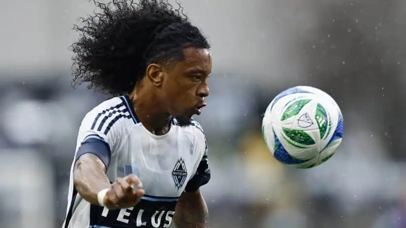 Vancouver Whitecaps Fc vs Los Angeles Football Club Picks and Predictions May 11th 2025 2 A soccer player in a white and navy jersey is skillfully kicking a colorful ball during a match under overcast skies.