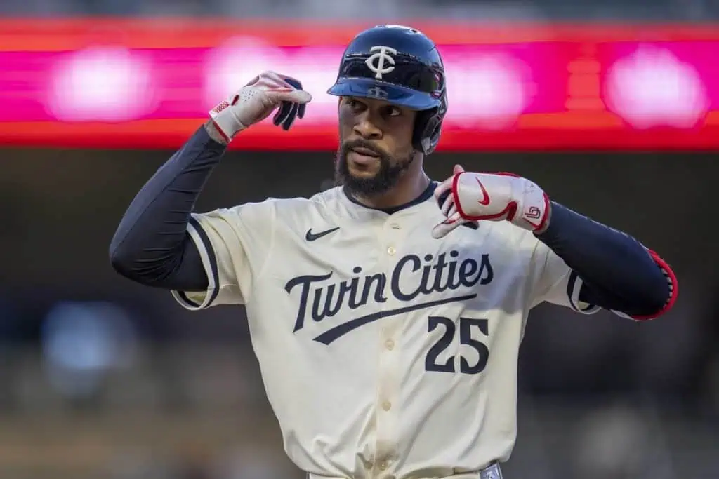 A baseball player in a "Twin Cities" jersey celebrates a play, gesturing confidently amid a vibrant stadium backdrop.