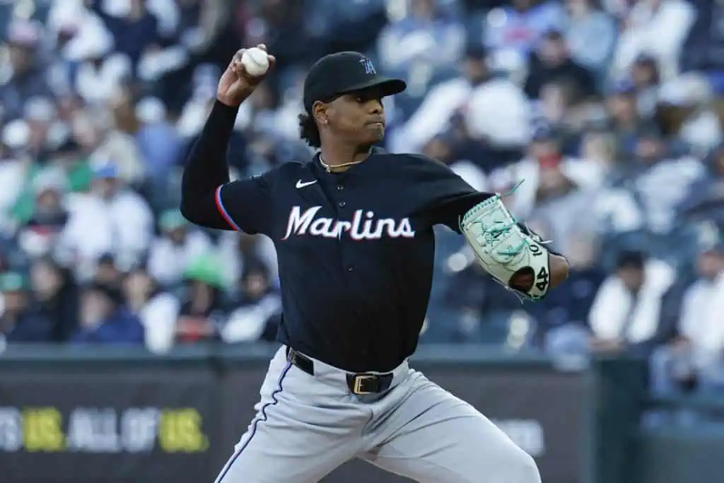 A Miami Marlins player in a black uniform is in the pitching stance, preparing to throw a baseball during a game with spectators in the background.