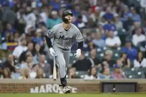 A player in a gray Miami Marlins uniform runs towards first base, bat in hand, with a blurred crowd in the background.