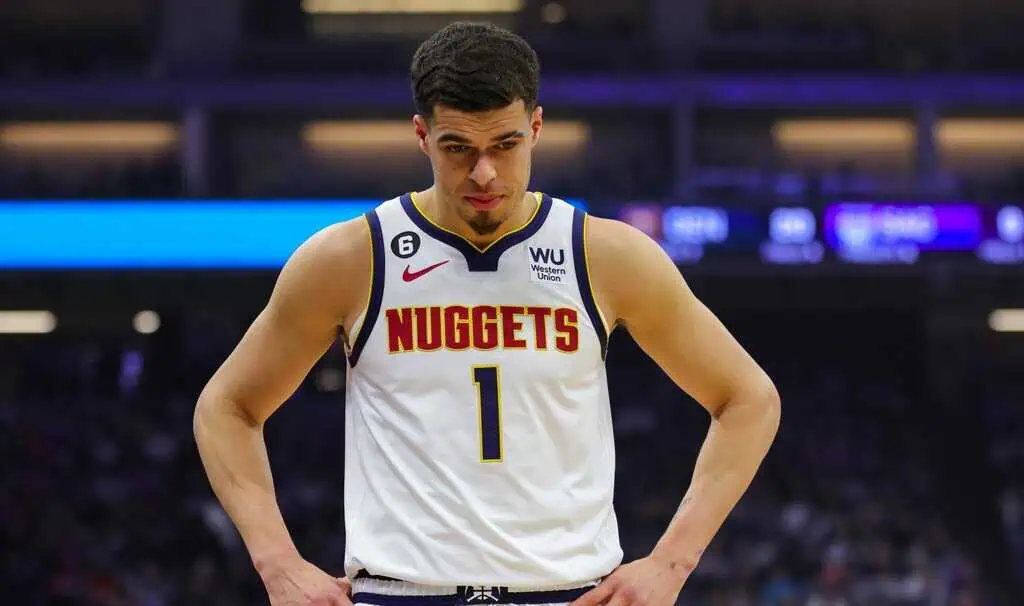 La Clippers vs Denver Nuggets Picks and Predictions May 1st 2025 2 A basketball player in a Denver Nuggets jersey stands with a focused expression on the court, surrounded by blurred arena lights.