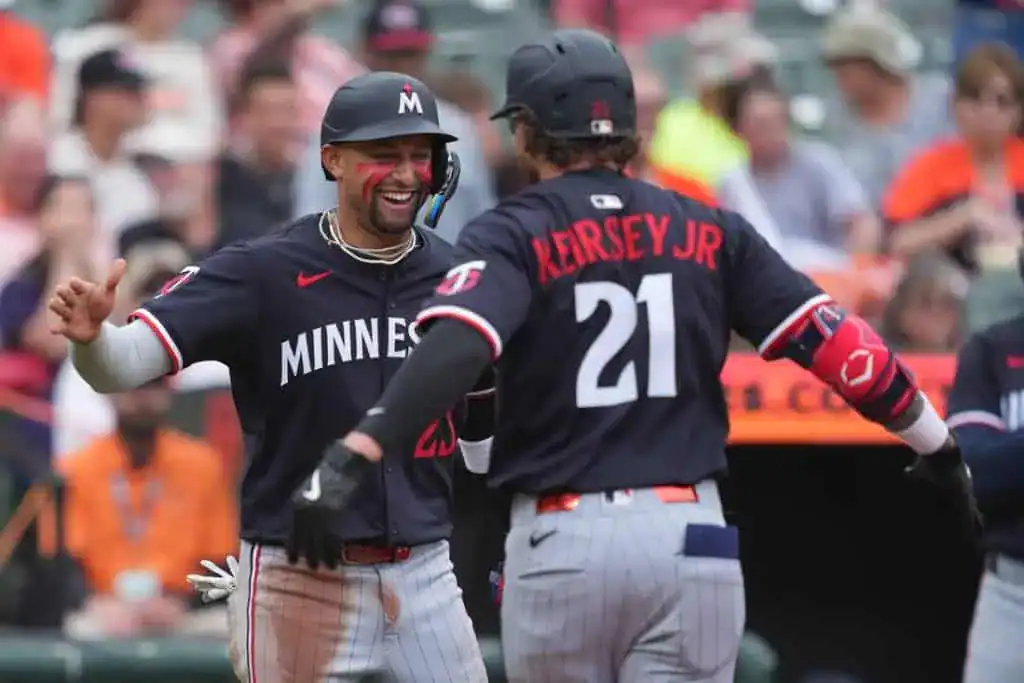 Two baseball players in Minnesota Twins uniforms celebrate a successful play on the field amidst a cheering crowd.