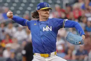 A baseball pitcher in a blue jersey delivers a pitch on the mound
