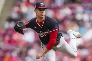 A pitcher in a navy and red baseball jersey, in mid-delivery, showcasing athleticism on a baseball field with a crowd in the background.