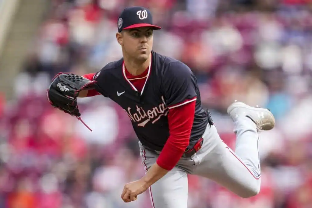 A pitcher in a navy and red baseball jersey, in mid-delivery, showcasing athleticism on a baseball field with a crowd in the background.