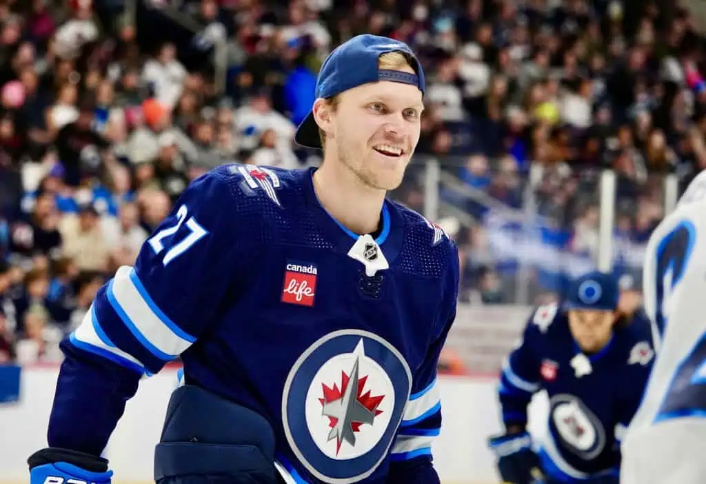 Dallas Stars vs Winnipeg Jets Picks and Predictions May 11th 2025 2 A hockey player in a blue Winnipeg Jets jersey stands on the rink, with a crowded audience visible in the background.