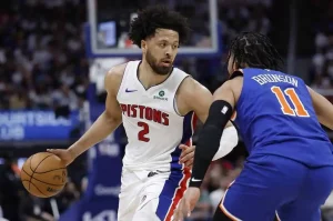 A Detroit Pistons player dribbles the basketball, closely guarded by a New York Knicks opponent during an intense game.