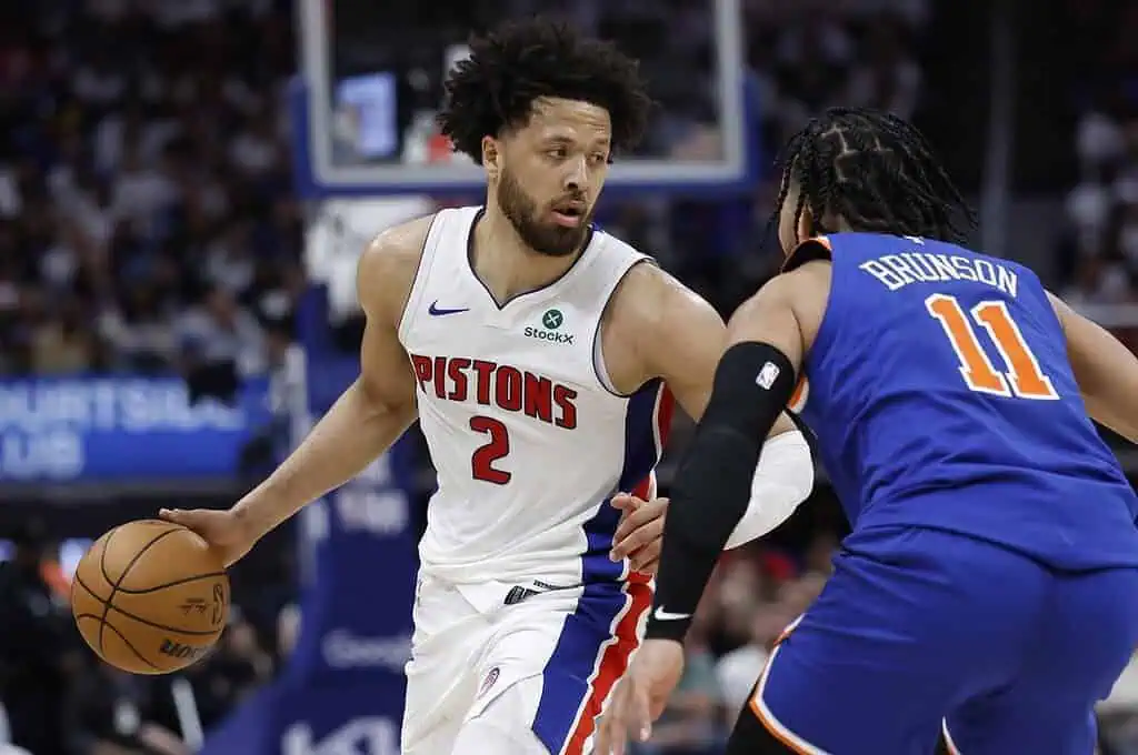 A Detroit Pistons player dribbles the basketball, closely guarded by a New York Knicks opponent during an intense game.