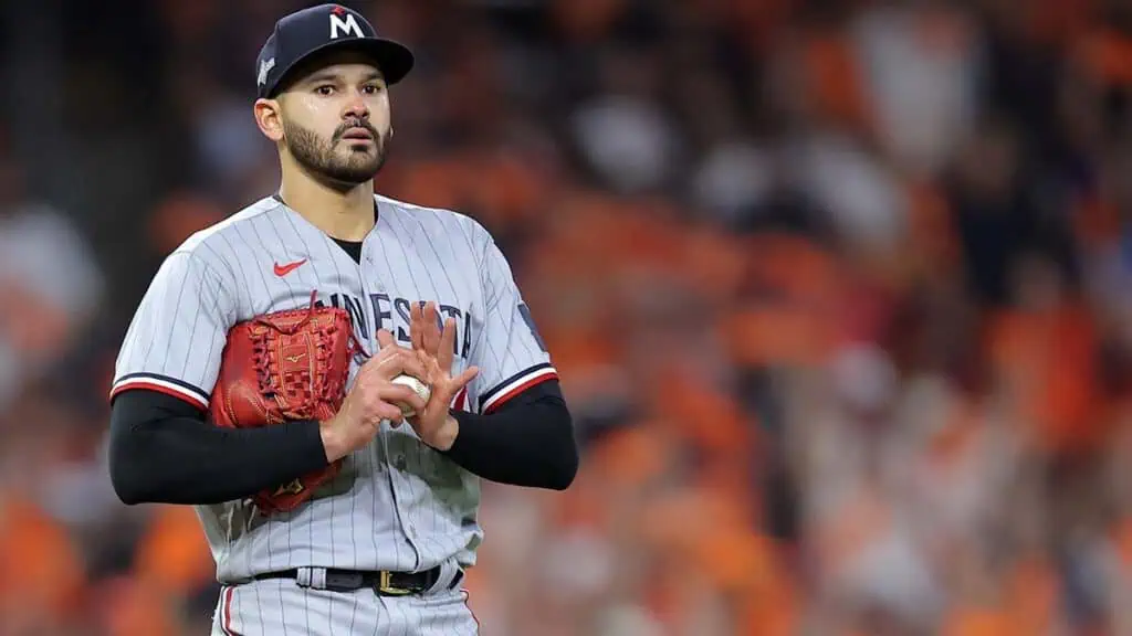 Minnesota Twins vs Baltimore Orioles Picks and Predictions May 6th 2025 2 A pitcher in a gray baseball uniform stands on the mound with a red glove, surrounded by an enthusiastic crowd dressed in orange.