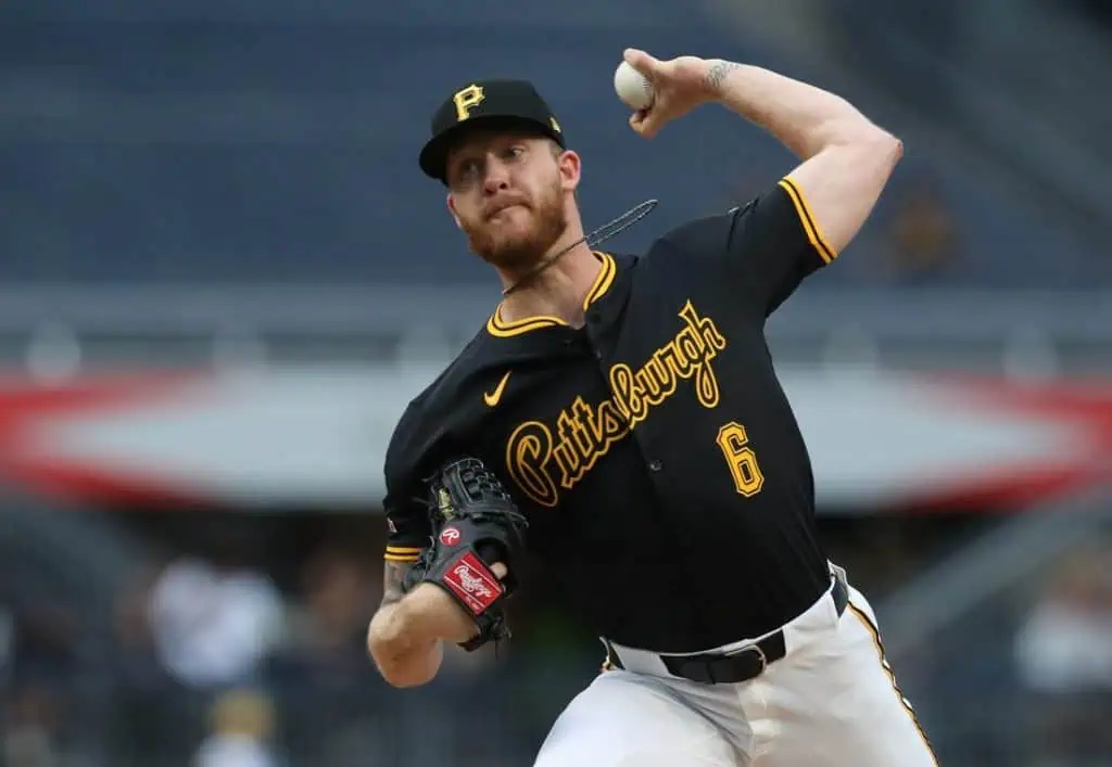 A baseball player in a black Pittsburgh Pirates jersey winds up to pitch, showcasing athletic form in a stadium setting.