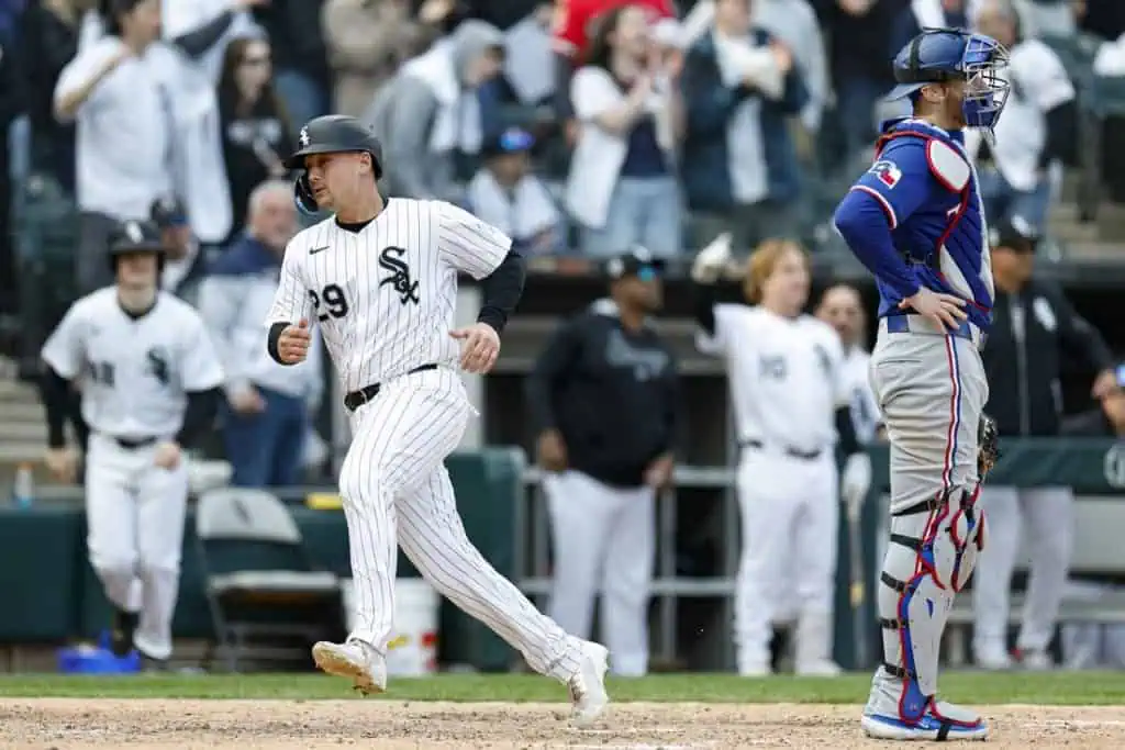 A Chicago White Sox player rounds the bases, celebrating a run, while a Texas Rangers catcher watches in disappointment, surrounded by cheering fans.