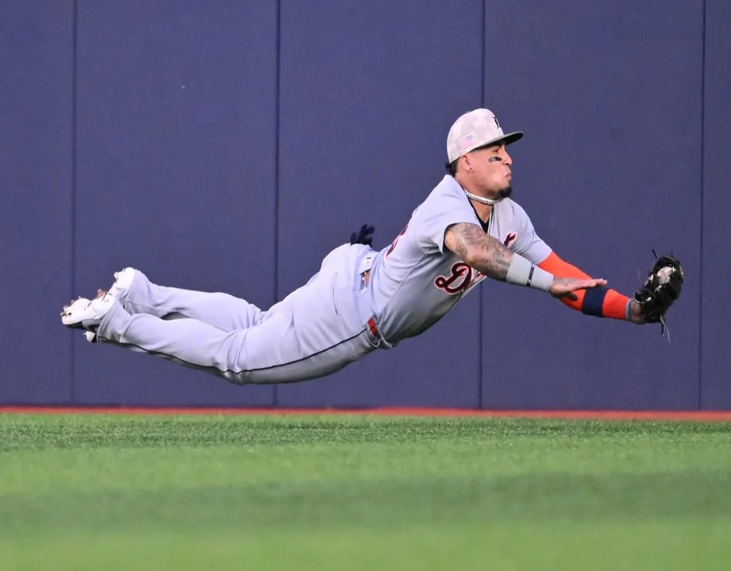 Detroit Tigers outfielder diving horizontally to catch a fly ball in front of the outfield wall