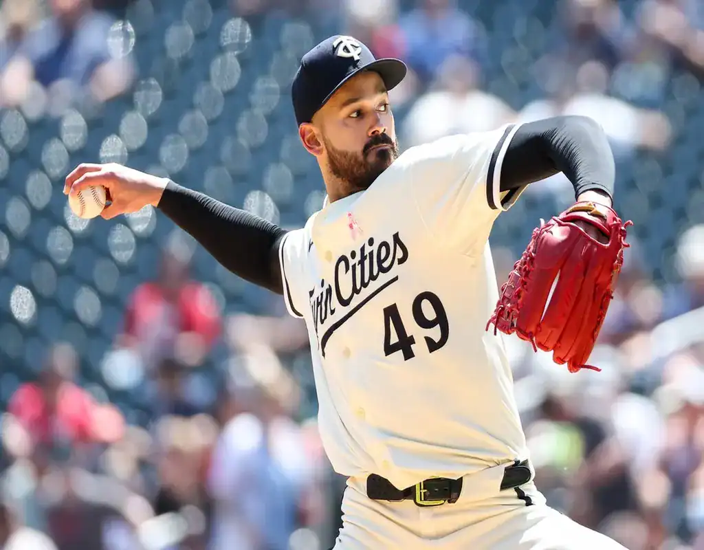 Minnesota Twins pitcher winding up for a pitch in a sunlit stadium with the crowd blurred behind him