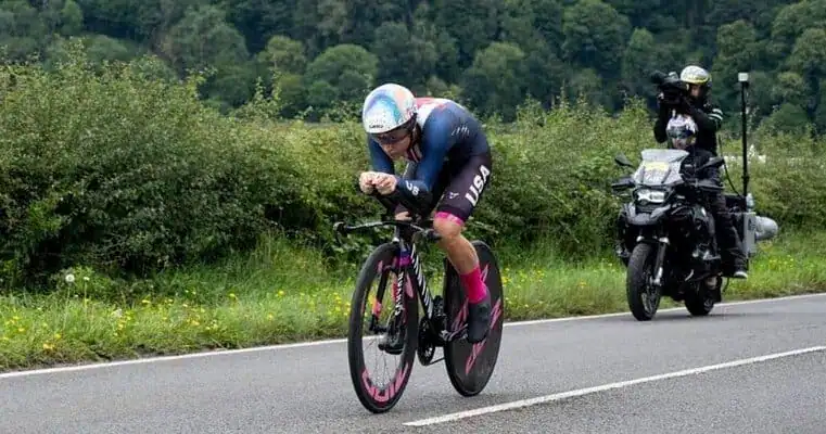 Ciclista compitiendo en la contrarreloj durante la carrera en ruta masculina, acompañado por motocicletas de seguimiento, en los Juegos Olímpicos de París 2024.