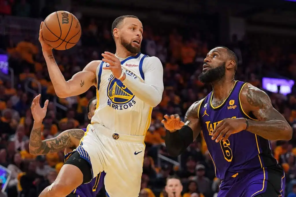 Houston Rockets vs Golden State Warriors Picks and Predictions May 4th 2025 2 A basketball player in a Warriors uniform prepares to pass the ball while two opponents from the Lakers closely defend him on the court.