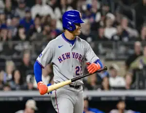 New York Mets batter smiling and holding his bat in the on-deck circle with a packed stadium behind him