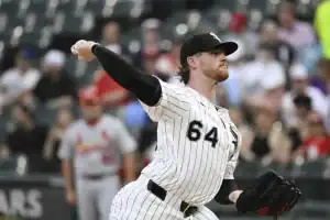 A pitcher in a striped white and black uniform winds up to throw a baseball
