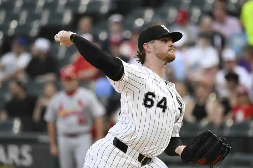 A pitcher in a striped white and black uniform winds up to throw a baseball