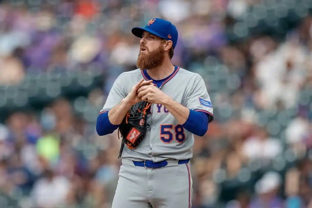 A pitcher in a gray New York Mets uniform, number 58, prepares to throw on the mound during a game with spectators in the background.