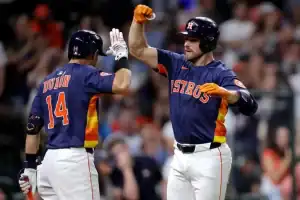 Two Houston Astros players celebrate a successful play, wearing vibrant team jerseys with orange and navy colors, in a lively stadium.