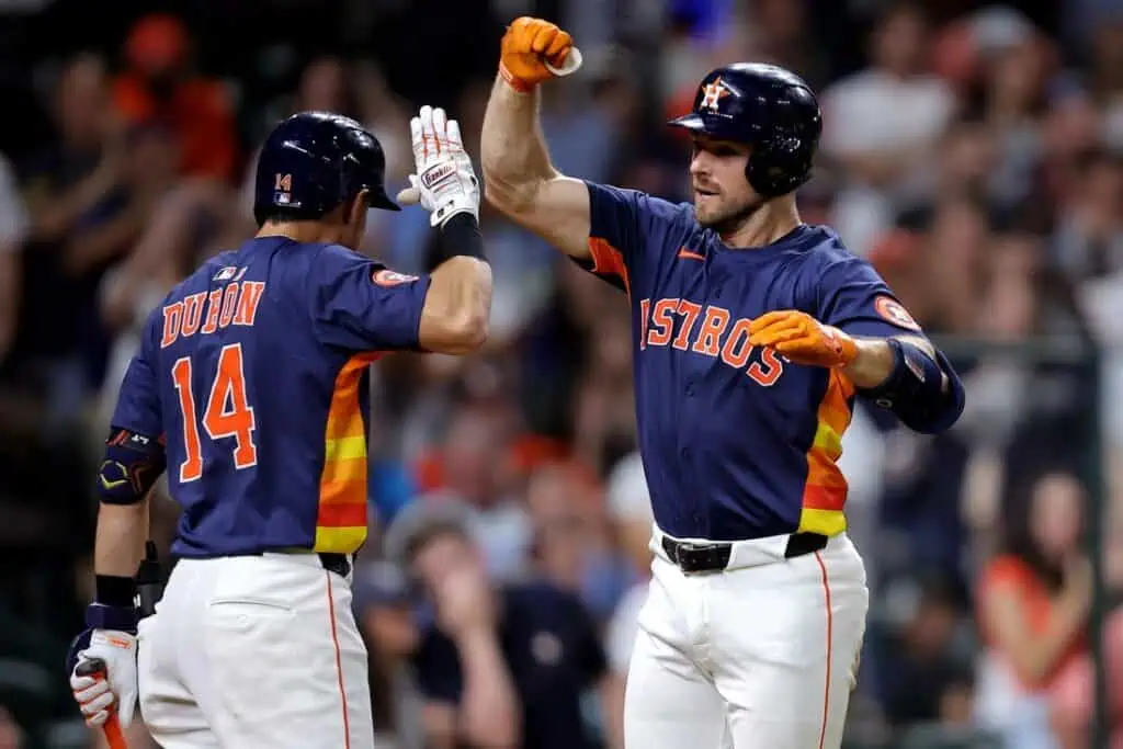 Two Houston Astros players celebrate a successful play, wearing vibrant team jerseys with orange and navy colors, in a lively stadium.