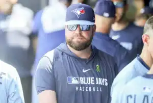 A group of baseball players wearing Toronto Blue Jays jerseys and team hats, gathered in a stadium's dugout area.