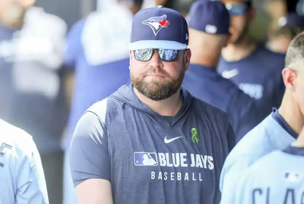 A group of baseball players wearing Toronto Blue Jays jerseys and team hats, gathered in a stadium's dugout area.