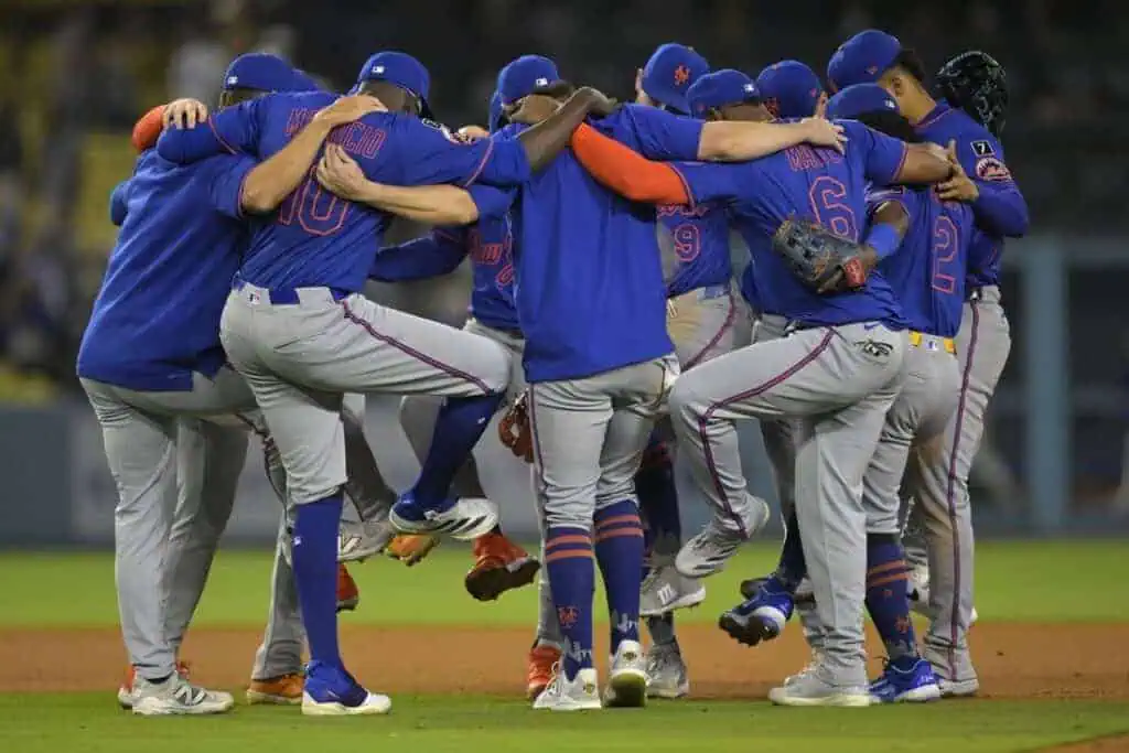A group of baseball players in blue jerseys huddle closely, celebrating in a lively, interconnected pose on the field.