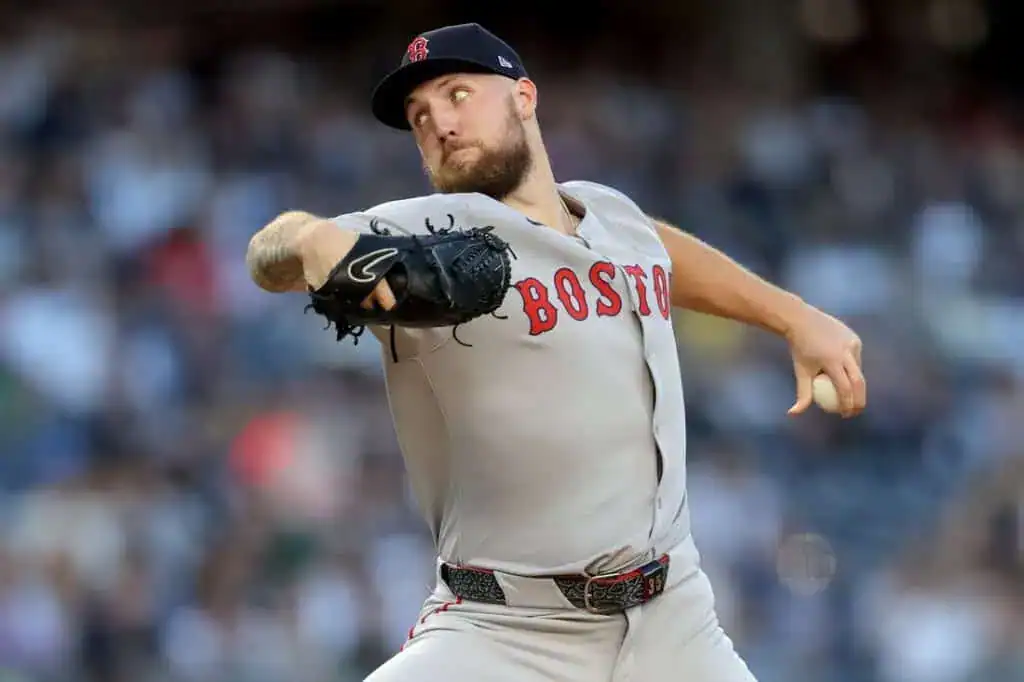 A Boston Red Sox player in a gray uniform prepares to pitch, showcasing a dynamic throwing motion against a blurred stadium backdrop.