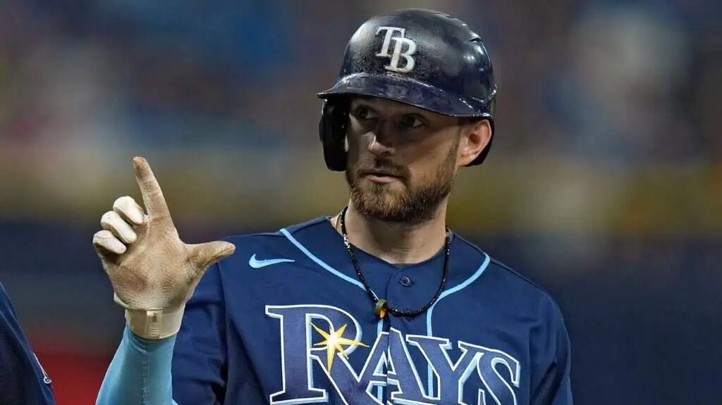 A baseball player wearing a Tampa Bay Rays jersey and helmet gestures with one hand while standing on the field.