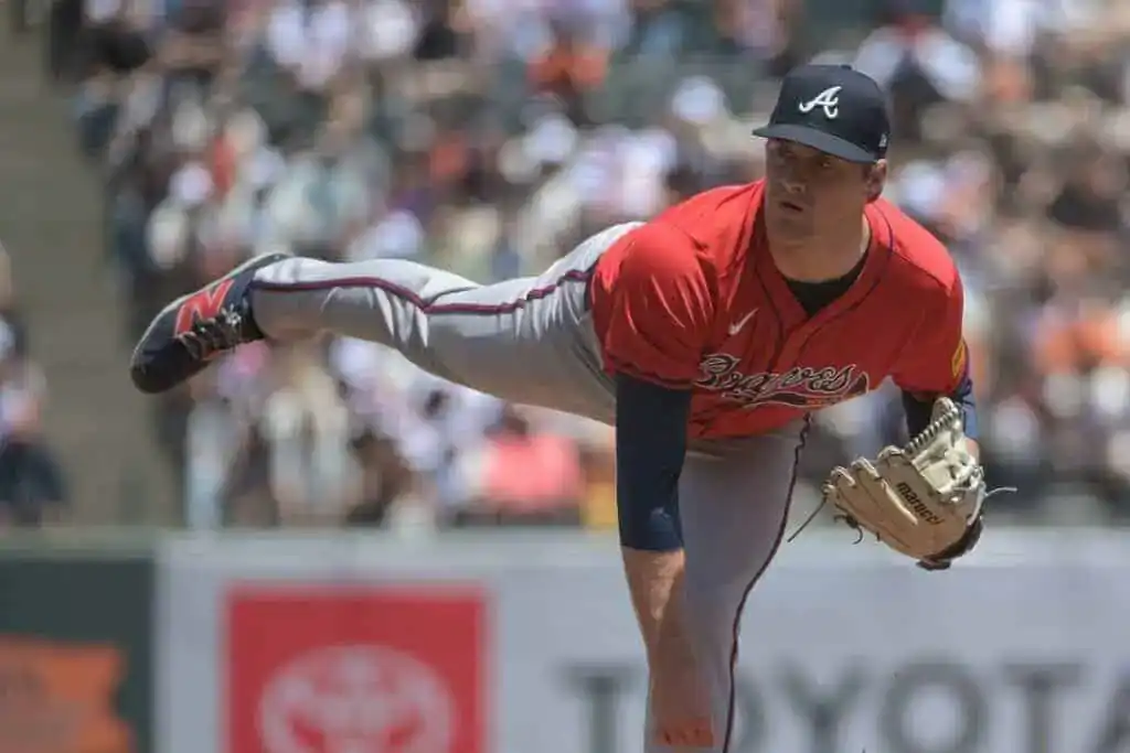 A pitcher in a red Braves uniform prepares to throw a baseball, showcasing intense focus amid a crowded stadium backdrop.
