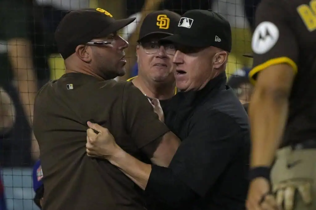 Two individuals in baseball attire appear to be engaged in a heated confrontation on the field. Tension is palpable among nearby spectators.